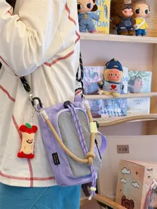 Vista dettagliata di una borsa a tracolla a quadri viola e grigia con ciondolo a forma di mela.
