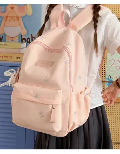 Detail view of the pink canvas school backpack with colorful bow embroidery and front pocket.