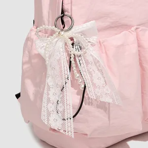 Foto de detalle de mochila rosa con elegante lazo de encaje blanco, perlas y prácticos bolsillos.