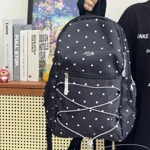 Detailed shot of casual black polka dot backpack with front bungee cords in cozy lifestyle scene.