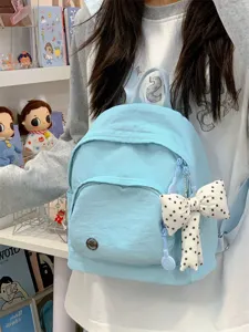 Detail shot of light blue mini backpack featuring polka dot bow charm in a cozy aesthetic scene.