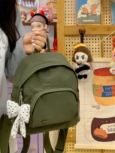 Close-up detail of dark green mini backpack with cute bow pendant in cozy room setting