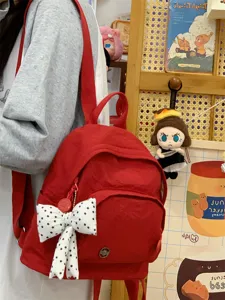 Red mini nylon backpack detail showing cute white polka dot bow charm and adjustable straps.