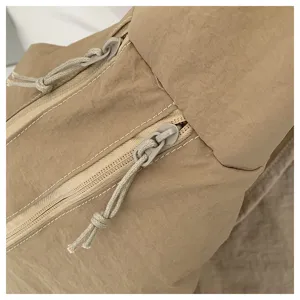 Close-up detail of khaki minimalist shoulder bag, fine white stitching and dual zippers.