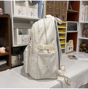 Seitenansicht eines weißen Rucksacks mit silbernem Sternenmuster, Seitentaschen und Riemen.