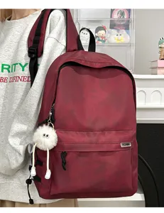 Close-up of maroon tie-dye backpack with fluffy eyeball keychain and front zipper pocket.