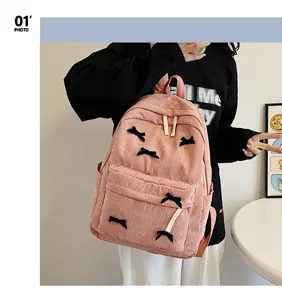 Pink corduroy backpack detail featuring cute black bows, front pocket, and adjustable straps.