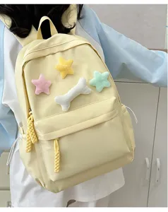 Detail view of cute yellow student backpack with plush star and bone charms for daily use.