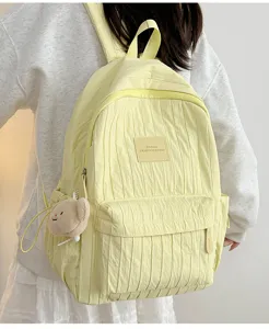 Detailed view of light yellow pleated backpack with front pocket and cute bear pendant.