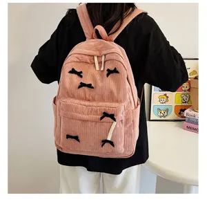 Cute pink corduroy backpack for women, stylish school bag with chic black bows and pockets.