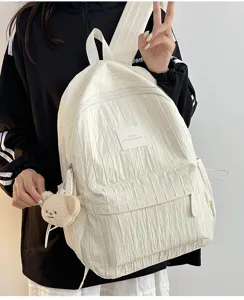 Detailed view of white nylon crumpled backpack with cute bear pendant and front pocket design.
