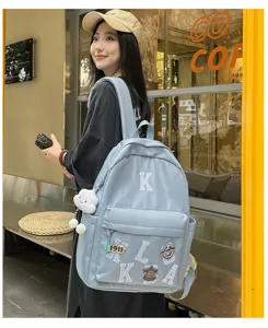 Detail view of casual blue school backpack with letter patches and cute pendant in street scene.