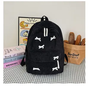 Close-up of black corduroy backpack featuring sweet white bow details and front pocket.