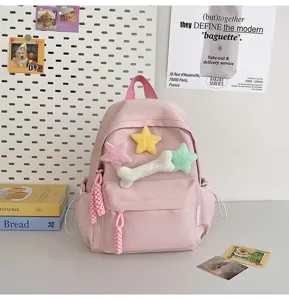 Pink student backpack detail view, featuring cute plush star and bone charms on canvas bag.