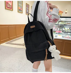 Close-up view of black corduroy backpack showcasing front pocket and cute bear pendant.