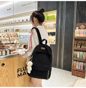 Black corduroy backpack lifestyle detail view with cute bear pendant in boutique store setting.