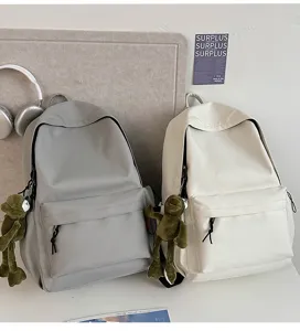 Minimalist solid color detail view of the school backpack featuring a cute frog plush pendant.