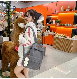 Detail shot of the grey corduroy backpack with a cute bear pendant in a cozy store scene.