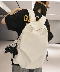 Detail shot of a minimalist white backpack with a cute monkey pendant, worn outdoors.