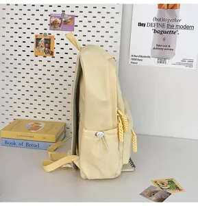 Side detail view of a stylish light yellow student backpack featuring braided zipper pulls on desk.