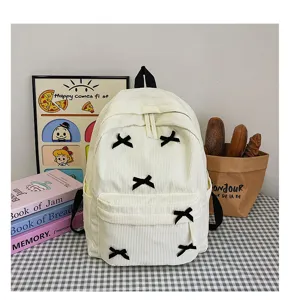 Detailed view of white corduroy backpack with cute black bow accents on checkered tabletop.