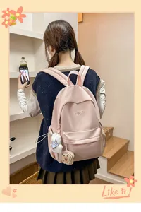 Casual pink student backpack detail view with cute plush pendants and smooth fabric.