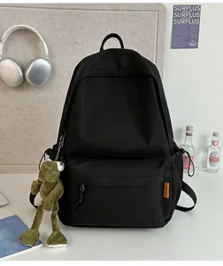 Minimalist black backpack detail featuring spacious main compartment and cute frog plush pendant.