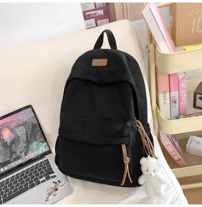 Black corduroy backpack detailed view, stylish student school bag with cute bear pendant.