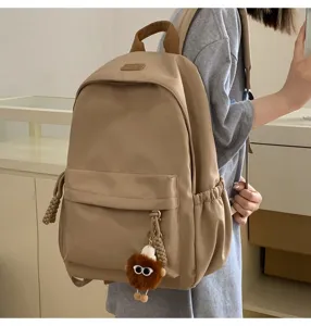 Detail view of the stylish khaki backpack worn by the model, highlighting pockets and plush charm.
