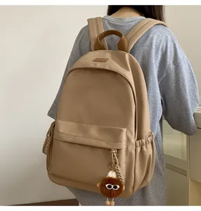 Detailed view of the casual beige school backpack with front pocket and cute plush charm.