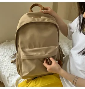 Detail view of a stylish beige nylon school backpack with a cute monkey keychain charm.