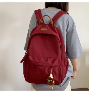 Stylish casual burgundy backpack with a cute doll pendant for school students daily use.