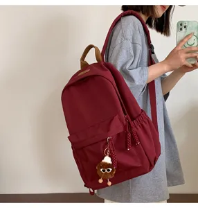Close-up detail of stylish casual burgundy backpack with top handle and cute plush keychain.