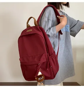 Detailed shot of a stylish burgundy canvas school backpack with brown handle and cute charm.