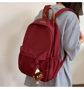 Stylish burgundy backpack for women, casual school bookbag with cute plush pendant.
