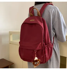 Detailed back view of a trendy maroon canvas backpack with brown top handle and cute charm.