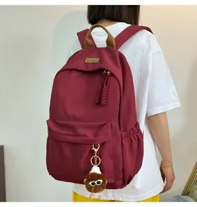 Detail shot of a stylish dark red canvas backpack with brown handle and cute plush charm.