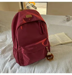 Casual burgundy school backpack with front pocket, cute plush pendant, and durable fabric.