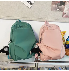 Close-up detail of casual minimalist school backpacks with cute monkey plush pendants.