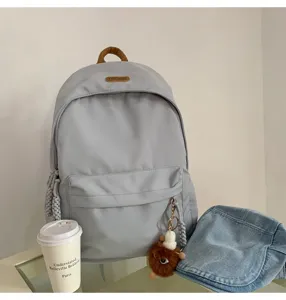 Detail view of stylish grey school backpack with front pocket and cute plush keychain charm.
