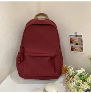 Burgundy casual daily backpack detail view with front zipper pocket and braided charms.