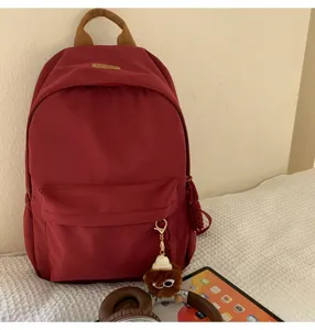 Detailed view of the stylish red backpack featuring front pocket and cute plush pendant charm.