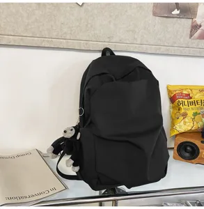 Detail shot of a black minimalist casual backpack with large capacity and cute monkey pendant.