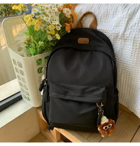 Detail view of casual black school backpack with front pocket and cute plush pendant charm.
