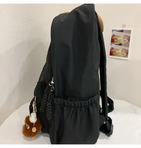 Side view detail of a classic black school backpack with side pocket and cute plush pendant.