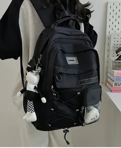 Detailed view of the utility-style black backpack with multiple pockets, elastic cords, and charm.