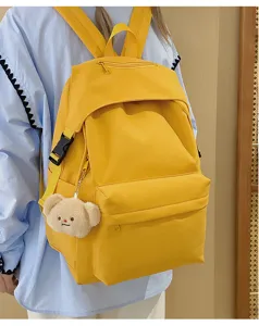 Yellow nylon casual school backpack detailed view with cute plush bear pendant on model back.
