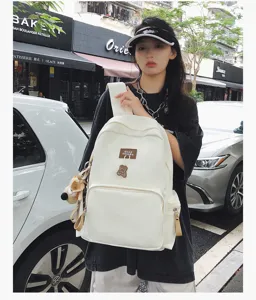 Outdoor detail view of a casual campus backpack with cute bear pendant and solid color style.