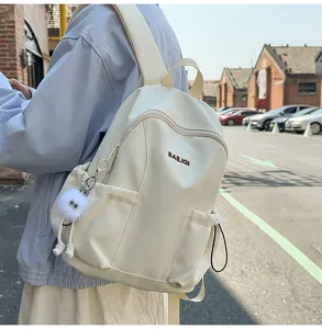 Detail shot of white casual backpack with front pocket and cute furry pendant outdoors.