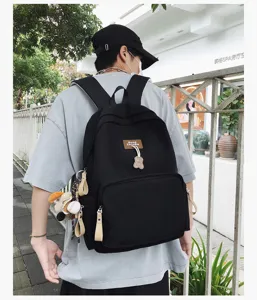 Detail shot of black campus backpack, featuring front pocket, bear pendant and casual style.